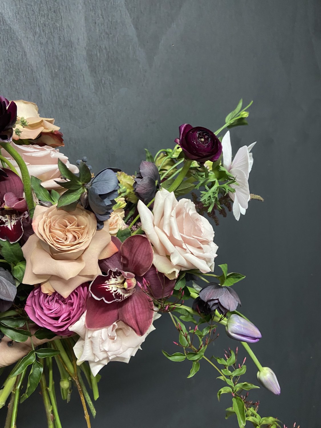 Dark, romantic bridal bouquet of roses, ranunculus and hellebore against a deep green wall