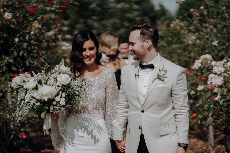 Bride and groom smiling in a rose garden, bride holding a loose white and green bouquet