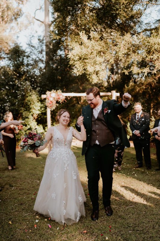 Newlyweds walking back down the aisle through confetti beneath a floral arch