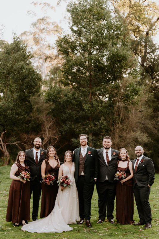 Bridal party in deep burgundy holding autumn-toned bouquets among gum trees