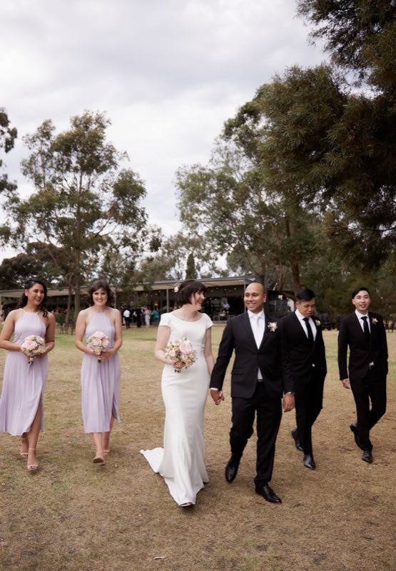 Bridal party in soft lilac walking across a lawn with pale posies